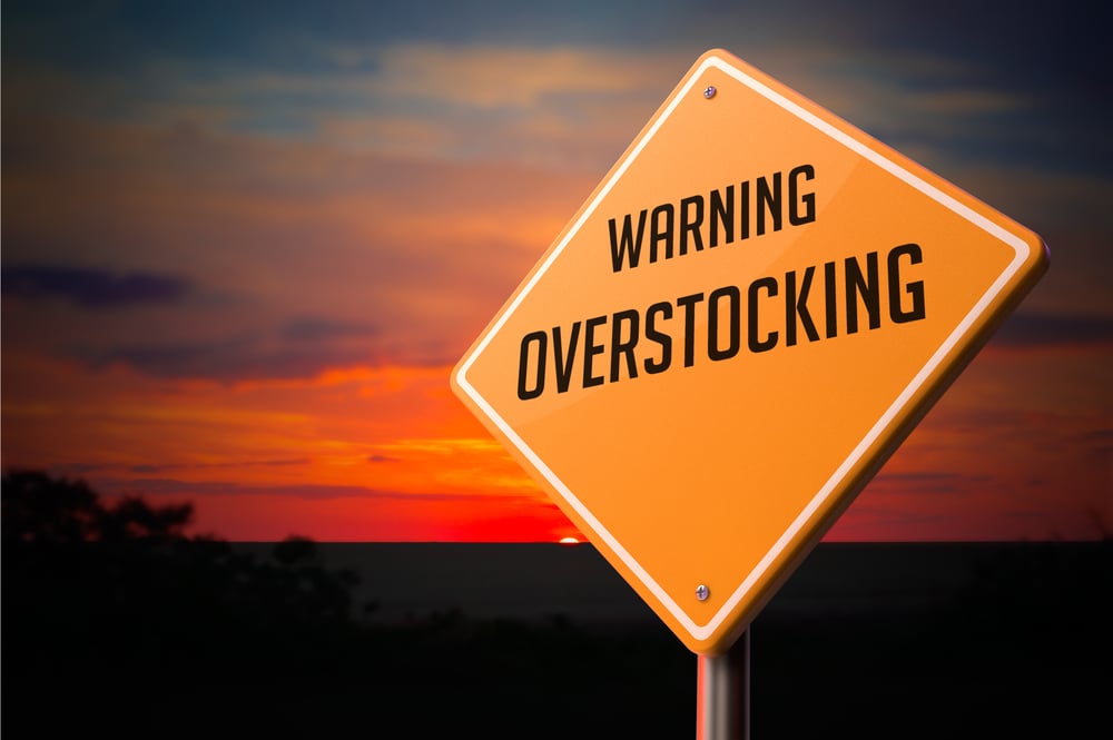 Overstocking on Warning Road Sign on Sunset Sky Background.