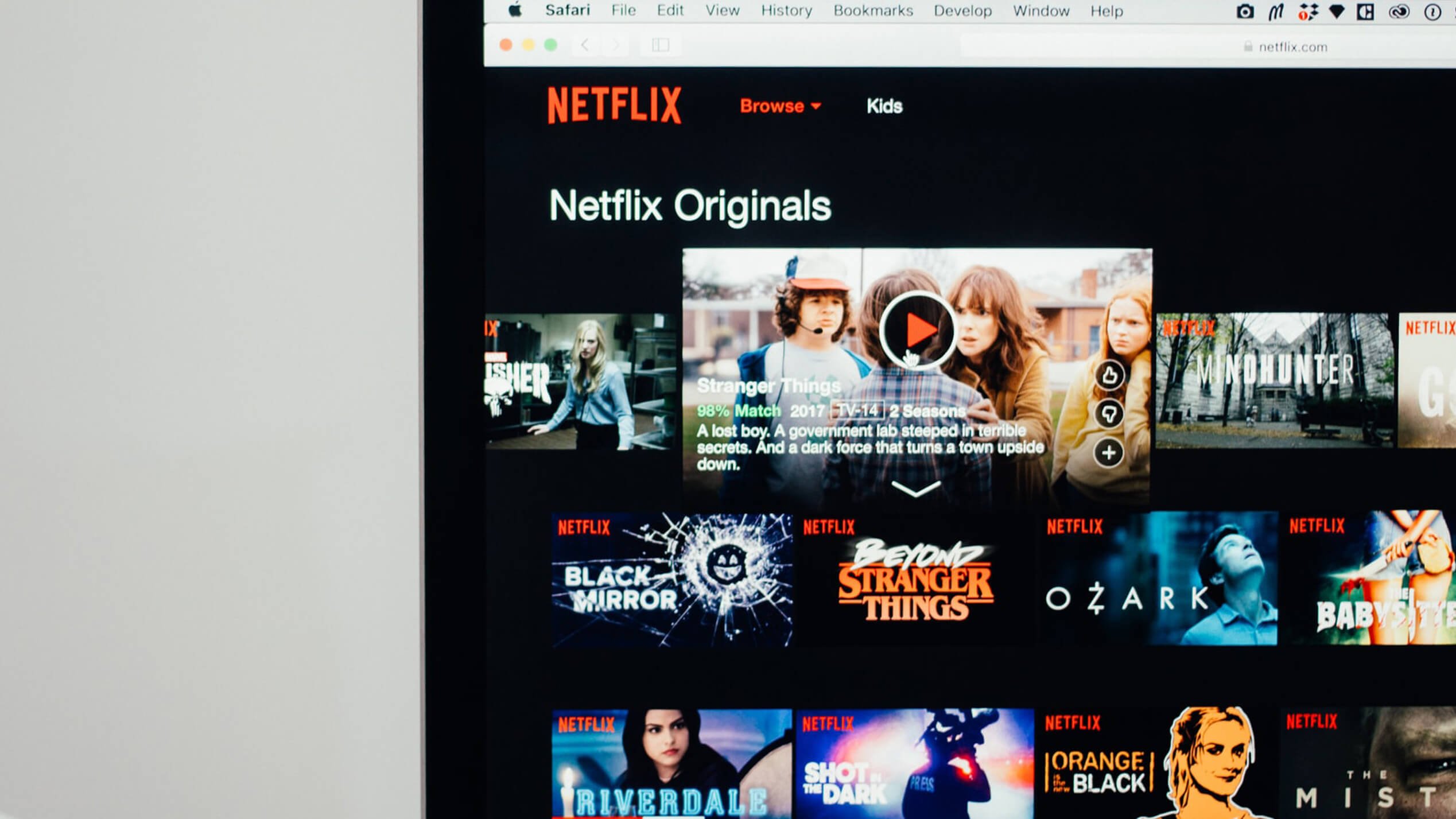 A laptop shows the Netflix browser displaying a grid of Netflix origin programs including Black Mirror and Stranger Things.